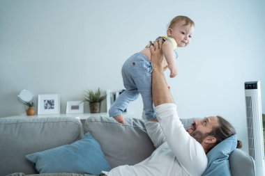 Kanepede oturan bir adam çocuğu kaldırıyor.