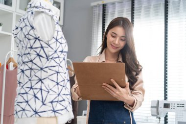 Asyalı terzi kadının portresi terzi atölyesinde giysiler üzerinde çalışıyor.
