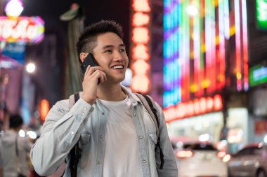 Canlı şehir ışıklarında akıllı telefondan konuşan gülümseyen adam.