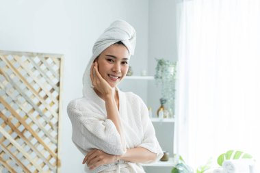 Banyoda beyaz bornoz ve havlu giymiş gülümseyen bir kadın.