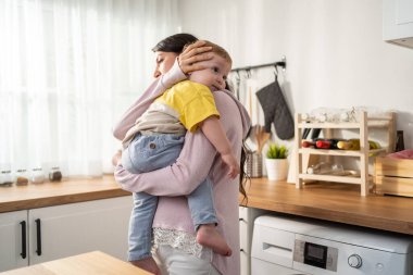 Kadın, çocuğu mutfakta ahşap tezgahın yanında tutuyor.