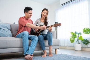 Birlikte oturan çift, parlak odada gitar çalıyor.