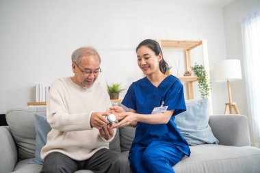 Asyalı genç bakıcı, tekerlekli sandalyedeki yaşlı adama dikkat et. Çekici hemşire doktoru yaşlı yetişkin erkek hastalara bakıyor. Bakımevinde reçeteli ilaç şişesini açıklıyor..