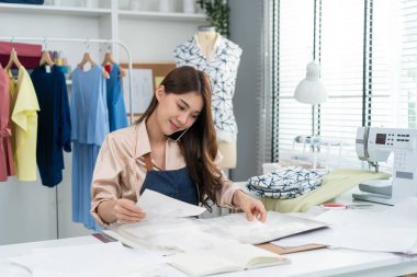 Asyalı güzel terzi kadın terzi atölyesinde giysiler üzerinde çalışıyor..