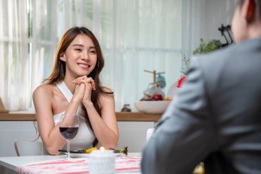 Kadın şarap kadehiyle masada otururken gülümsüyor.