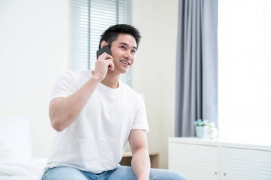 Yakışıklı Asyalı genç adam yatak odasında cep telefonu kullanıyor.