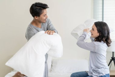 Asyalı genç ve güzel bir çift yatakta yastık savaşı yapıyor..