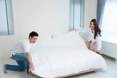 Asyalı genç çift sabah birlikte uyandıktan sonra battaniye katlıyor. Çekici yeni evli erkek ve kadın pijamalarıyla mutlu olurlar ve evde yatak odasından birlikte kalktıktan sonra rahatlarlar..