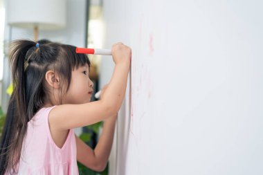 Asian young sibling kid girl enjoy paint on white wall in living room. Little adorable children having fun drawing and coloring art picture with hapiness enjoy creativity activity on holiday at home.