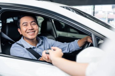 smiling asian male in suit showing car keys to new car showroom