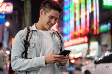 Gülümseyen adam şehrin caddesinde dururken akıllı telefon kullanıyor.