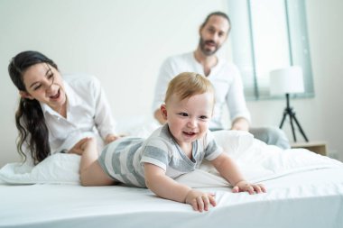 Aileler mutlu bir şekilde izlerken gülümseyen bebek yatakta emekliyor.