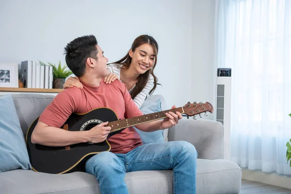 Erkek gitar çalarken kadın gülümsüyor ve yanında oturuyor.