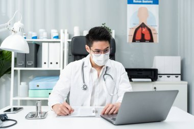 Masa başında dizüstü bilgisayar kullanan bir doktor.