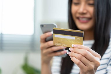 Evde akıllı telefon kullanan bir kadın kredi kartı tutuyor.