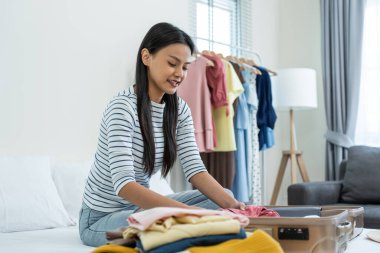 Genç bir kadın yatakta otururken elbiselerini katlıyor.