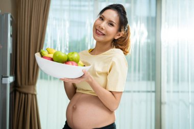 Elinde taze meyvelerle gülümseyen hamile kadın.