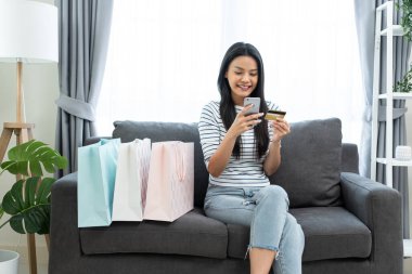 Kanepede oturan kadın akıllı telefon ve kart kullanırken gülümsüyor.