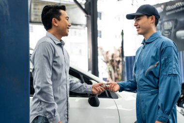Car mechanic returns car keys to owner in workshop