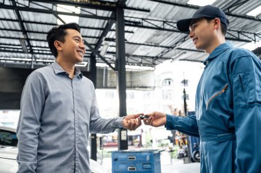 Car mechanic returns car keys to owner in workshop