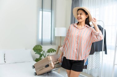 Modern yatak odasında bavulu tutan kadın gülümsüyor.