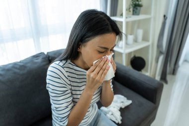 Kanepede oturmuş peçeteyle burnunu siliyor.