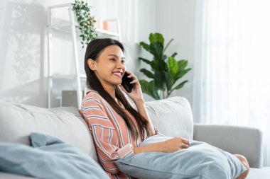 Kanepede oturmuş akıllı telefondan konuşan gülümseyen kadın.