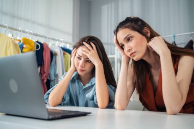 Two women sitting at table looking stressed using laptop