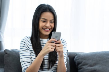 Kapalı alanda akıllı telefon kullanan gülümseyen bir kadın.