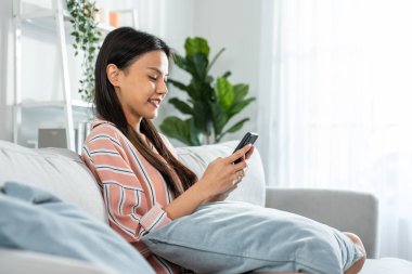 Woman sitting on sofa using smartphone and smiling happily