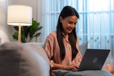 Kanepede oturan kadın rahat oturma odasında dizüstü bilgisayar kullanıyor.