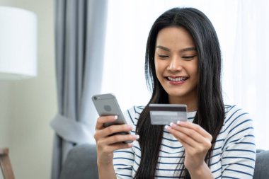 Evde akıllı telefon kullanan, elinde kredi kartı tutan gülümseyen kadın.