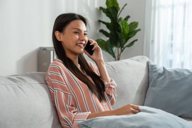 Kanepede otururken akıllı telefondan konuşan gülümseyen kadın.