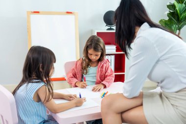 Beyaz tenli güzel bayan öğretmen okuldaki çocuklara resim öğretiyor. Çekici eğitmen kadın, anaokulunda resim çizmeyi ve resim yapmayı öğretiyor..