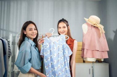 Butikte elinde elbiseyle gülümseyen iki kadın.