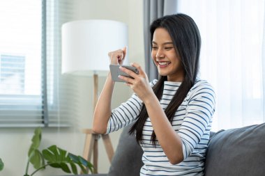 Kanepede oturan gülümseyen kadın mobil oyun oynuyor.