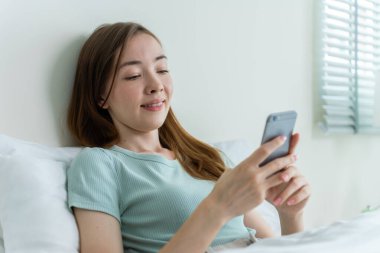 Beyaz bir kadın sabahları cep telefonu sohbetini evde yapıyor. Mutlu, sıradan, güzel bir kadın yatak odasında oturmuş, hafta sonunun keyfini çıkarıyor, akıllı telefon kullanarak evdeki teknolojiyle iletişim kuruyor..