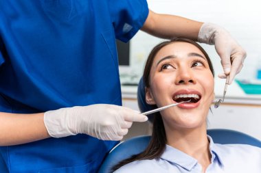 Beyaz dişçi diş sağlığı kliniğindeki genç kız için dişleri muayene ediyor. Diş hekimliği koltuğunda yatan çekici kadın hastanede muayene sırasında doktordan diş tedavisi görüyor.