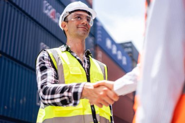 Konteynır limanında çalışan iş kadını ve erkek işçiye yakın çekim. Çekici kadın ve erkek, kargo gemisindeki depo lojistik terminalinde işlemler yapıldıktan sonra el sıkışıyor.