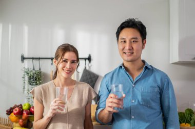 Asyalı çekici çift evde mutfakta bir bardak su içiyor. Genç, susamış adam ve kadın, sabah kalktıktan sonra bardakta temiz mineral tutuyorlar ve evde sağlık hizmetleri için yudumluyorlar..