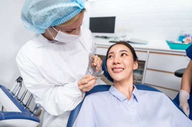 Beyaz dişçi diş sağlığı kliniğindeki genç kız için dişleri muayene ediyor. Diş hekimliği koltuğunda yatan çekici kadın hastanede muayene sırasında doktordan diş tedavisi görüyor.