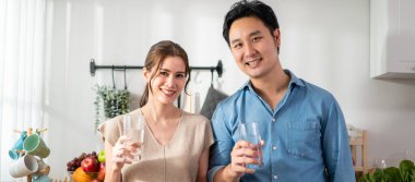 Asyalı çekici çift evde mutfakta bir bardak su içiyor. Genç, susamış adam ve kadın, sabah kalktıktan sonra bardakta temiz mineral tutuyorlar ve evde sağlık hizmetleri için yudumluyorlar..