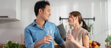 Asyalı çekici çift evde mutfakta bir bardak su içiyor. Genç, susamış adam ve kadın, sabah kalktıktan sonra bardakta temiz mineral tutuyorlar ve evde sağlık hizmetleri için yudumluyorlar..