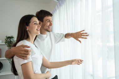 Mutlu genç çift sarılıyor, yan yana duruyor ve pencereye bakıyor.