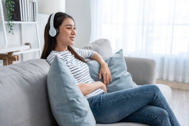 Asyalı kadın kanepede otururken müzik ve dans dinler. Çekici genç kız kulaklığını taktı ve evde boş zaman geçirmekten ve hafta sonu aktivitelerinin keyfini çıkarmaktan mutlu oldu..