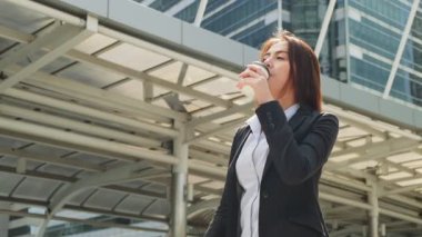 Asyalı genç ve zeki iş kadını şehirde yürüyor. Elinde kahve fincanı tutan kadın çalışma odasına doğru yürüyor.