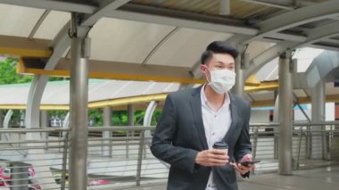 Adam elinde kahve ve telefon tutarken yürüyor.