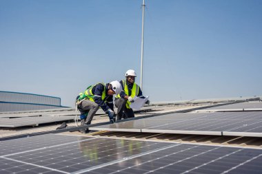 Profesyonel mühendis fotovoltaik panel sisteminin bakımı için çalışıyor. Çatı teftişi yapan çekici teknisyen güneş pili ekipman kutusunu gün batımında güneş pili alanında inceleyip kontrol ediyor.