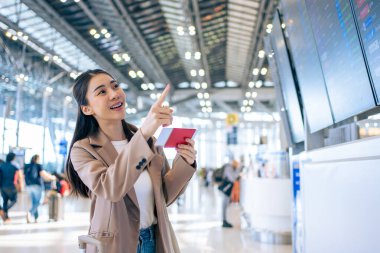 Asyalı genç bir kadın yolcu havaalanından geçiş kartını kontrol ediyor. Çekici güzel bayan turist arkadaşları tatil gezisi için uçakla yurtdışına gitmekten mutlu ve heyecanlı hissediyorlar..