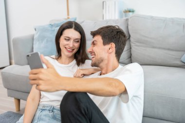 Beyaz tenli çekici çift oturma odasında cep telefonuyla konuşuyor. Çekici erkek ve kadın kendilerini mutlu ve rahat hissediyorlar. Sabahları akıllı telefondan sanal konuşmanın tadını çıkarıyorlar..